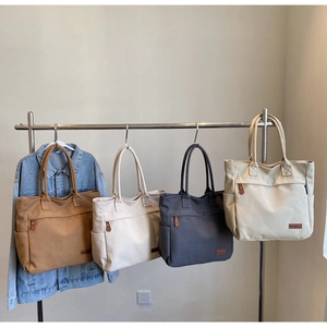 Row of large canvas tote bags in brown, beige, and grey hanging on a metal rack