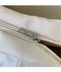 Detail shot of the polished silver metal zipper pull on a white canvas shoulder bag