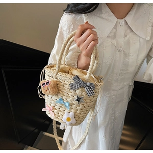 Détail du sac seau en paille avec décor d'ours en peluche et nœud à carreaux