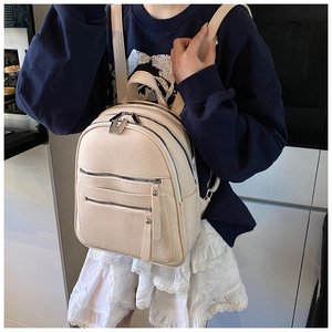 Detail of beige lychee leather backpack showing multi-zipper pockets and texture