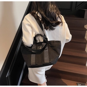 Détail d'un sac cabas en denim noir avec bandoulière réglable porté par un mannequin