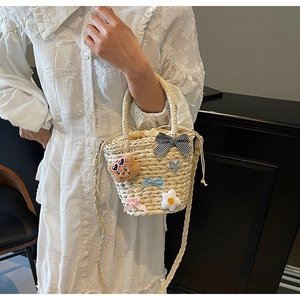 Détail d'un sac seau tissé avec un ours en peluche, des nœuds et des breloques fleurs