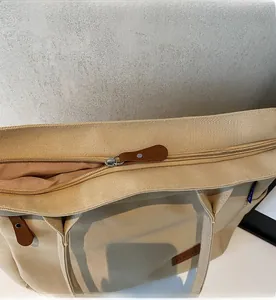 Detail of smooth metal zipper and brown leather handle on large beige canvas tote bag