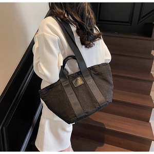 Détail d'un grand sac fourre-tout noir avec de larges sangles en nylon et un logo en cuir