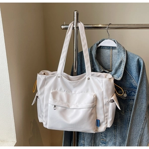 Detail of white nylon tote bag showing front zipper pocket and yellow drawstring side pocket