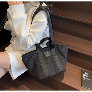 Détail d'un cabas en denim noir avec écusson logo en cuir et double bandoulière