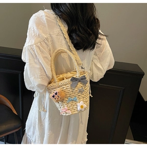 Détail du sac seau en paille avec ours en peluche, marguerites et nœud à carreaux