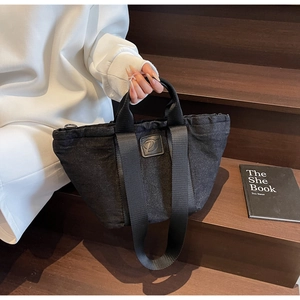 Détail du sac cabas en denim noir avec patch logo en cuir et large bandoulière durable