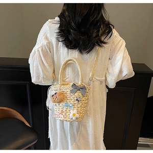 Détail d'un sac seau en paille tissé main avec ours en peluche et ornements de fleurs