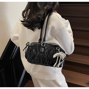 Detail of black pleated leather bowling bag with pearl lace bow charm on shoulder strap