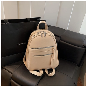 Detailed view of beige pebble leather backpack with multiple zipper pockets on a bench