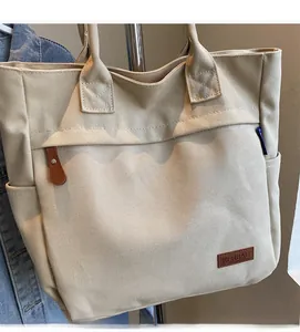 Detail view of cream canvas tote bag featuring front pocket and brown leather buckle strap