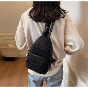 Detail of black crossbody chest bag featuring a colorful jacquard strap and zip pockets