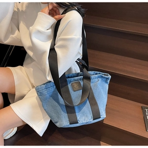 Détail du sac cabas en denim avec sangles noires et logo en cuir sur un escalier