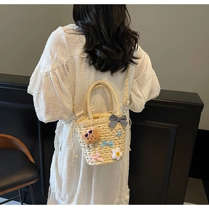 Détail du sac seau en paille tressée avec breloques mignonnes et nœuds décoratifs