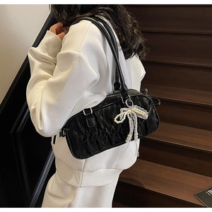 Detail of black pleated shoulder bag with pearl bow pendant on a white sweater background