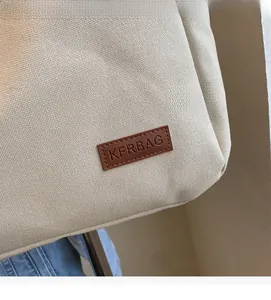 Close-up of beige canvas tote bag material with premium brown leather logo patch detail