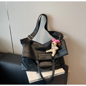 Detalle de bolso tote en cuero negro de grano suave con un colgante de perro blanco