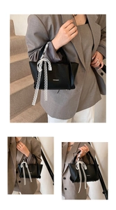 Detail of black pebbled leather handbag with white lace bow and sturdy handles
