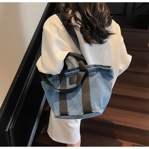 Détail d'un cabas en denim bleu avec sangles noires sur un escalier en bois