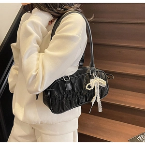 Detail of black pleated bowling bag with white lace bow and pearl charm on shoulder strap