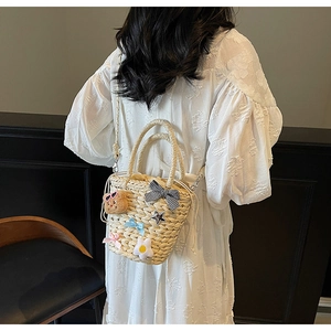Détail d'un sac de plage en paille avec ours en peluche et nœud sur une robe blanche