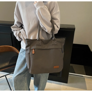 Detail of dark grey canvas tote bag featuring side pockets and a leather zipper pull