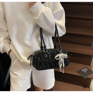 Close-up of black pleated Boston bag with long handles and pearl lace bow charm