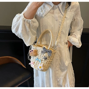 Détail d'un sac seau en paille avec ours et nœuds sur une robe en dentelle blanche