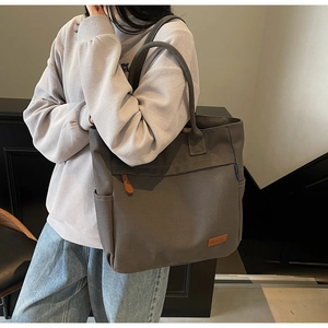 Detail of grey canvas tote bag showing the side pocket and brown leather logo patch
