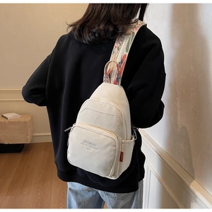 Detail of cream nylon chest bag with embroidered jacquard strap on minimalist background