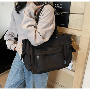Detail of black canvas tote bag showing front zipper pocket and side drawstring storage