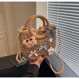 Détail d'un sac seau en paille avec breloque ours en peluche et rubans colorés