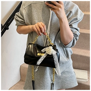 Detail of black faux leather bag featuring a gold chain handle and white lace bow accessory