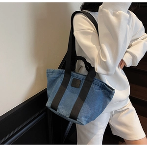 Détail du sac cabas en denim bleu avec anses en sangle noire et patch en cuir embossé