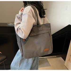 Detail of dark grey canvas tote bag with brown leather brand tag and side pocket