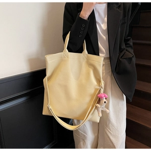 Detalle de bolso tote amarillo crema con textura lichi y colgante de perro de peluche