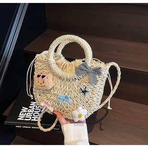 Détail du sac en paille avec ours mignon, nœud damier et breloques sur escalier en bois