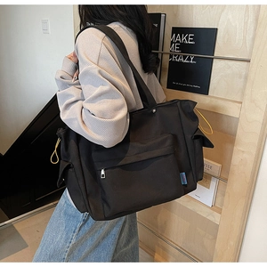 Detail of black multi-pocket tote bag with yellow drawstring and blue side tag label