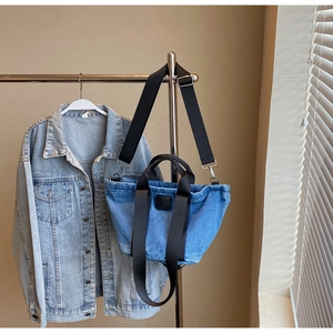 Détail du sac cabas en denim bleu avec sangle en nylon noir réglable et logo patch