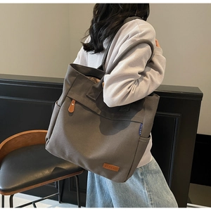 Detail of spacious dark gray canvas tote showing leather tag and side pocket for commute