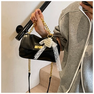 Detailed shot of black leather handbag featuring gold chain and pearl bow decoration