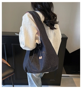 On-body shot of a large blue denim tote bag with visible stitching and front pocket detail