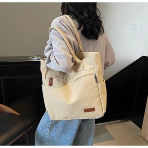 Detail of a large beige canvas tote bag with side pocket and brown leather brand label