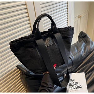 Détail du sac cabas en denim noir avec patch logo en cuir et bandoulière large
