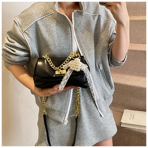 Detail of black leather crossbody bag with gold chain and white lace pearl charm