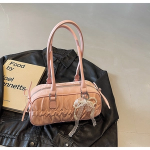 Detailed view of pink pleated handbag with lace bow and pearl charm on leather background