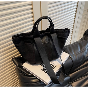 Détail d'un sac cabas en denim noir avec patch logo en cuir sur un canapé