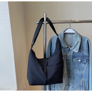 Detail view of a black nylon crossbody bag featuring an adjustable strap and front pocket