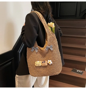 Détail d'un sac cabas en paille tissée avec nœuds à carreaux et pendentifs ours en peluche